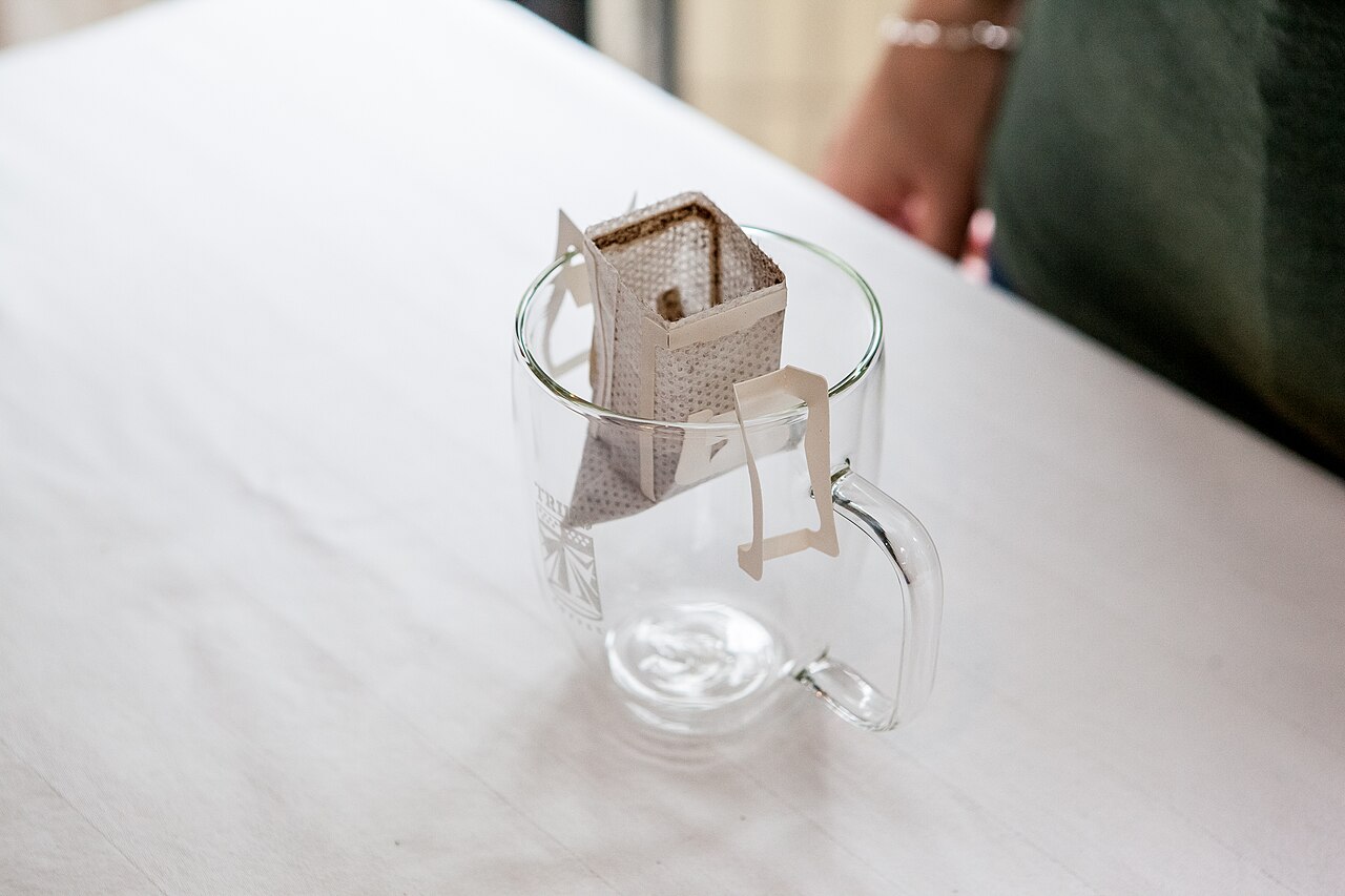 Step-by-step preparation of coffee in wooden pilón, hands pounding beans with rhythmic motion, rustic kitchen