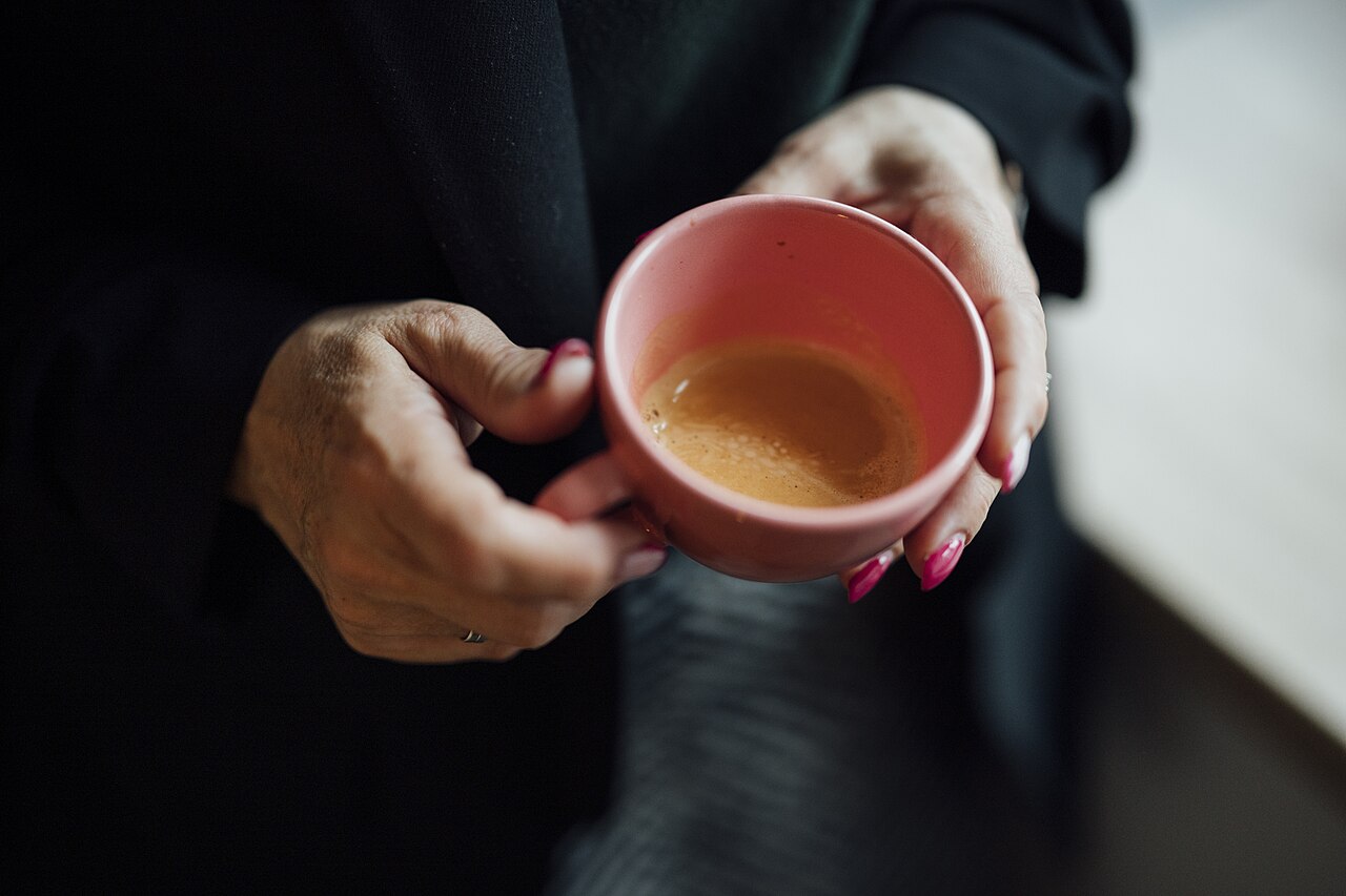 Person holding small cup of black coffee thoughtfully, close-up, contemplative mood, savoring the flavor