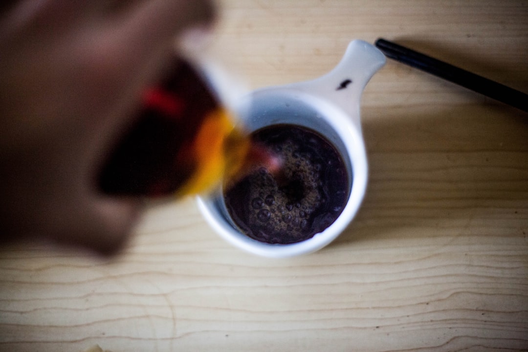 Coffee syrup being prepared on stovetop, dark thick liquid reducing in a saucepan, brown sugar and coffee beans nearby