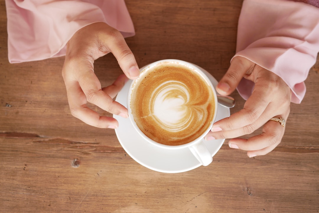 hands cradling a black Café Madre Isla coffee bag, roasted coffee beans spilling out, a Puerto Rican mountain landscape backdrop visible through a window
