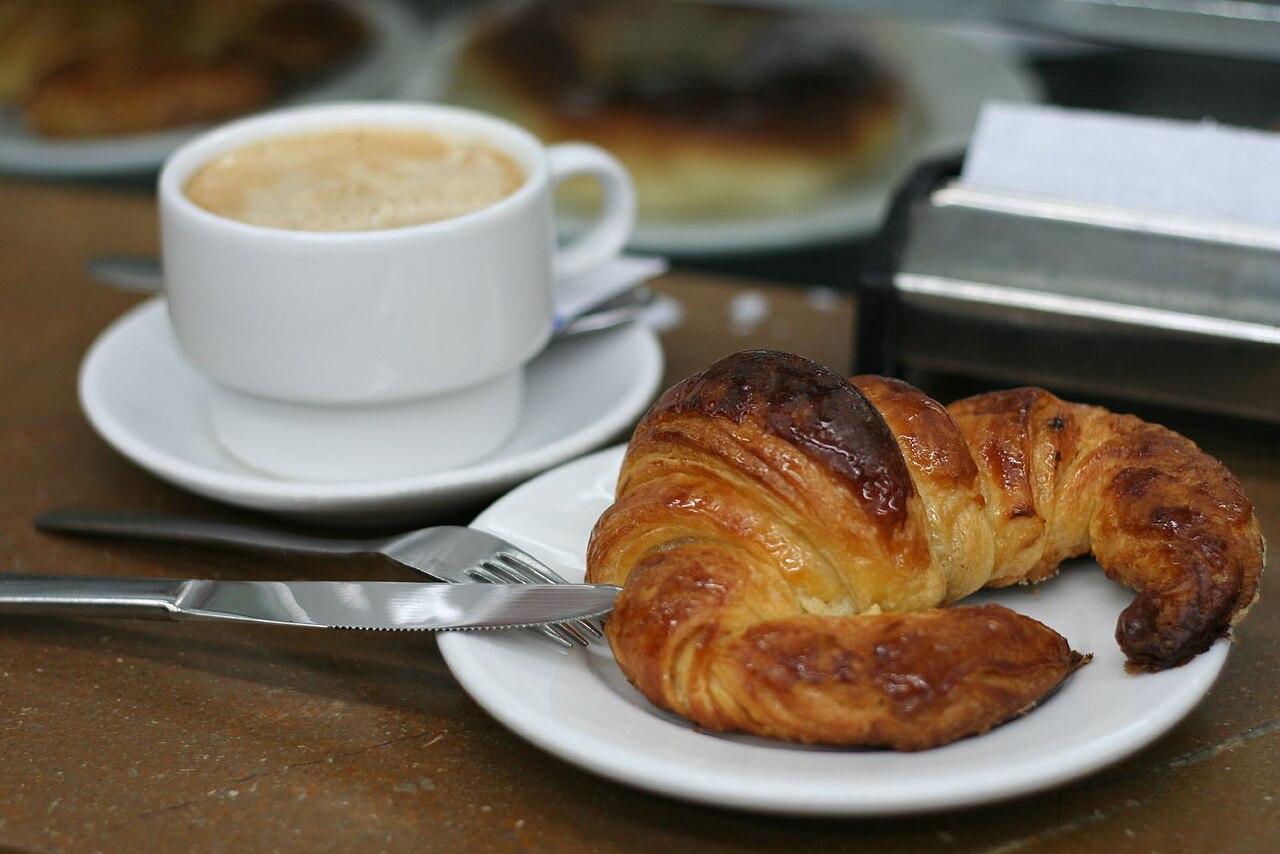 Traditional Puerto Rican café con leche in a white ceramic cup on a wooden table, steam rising, morning sunlight, warm kitchen setting