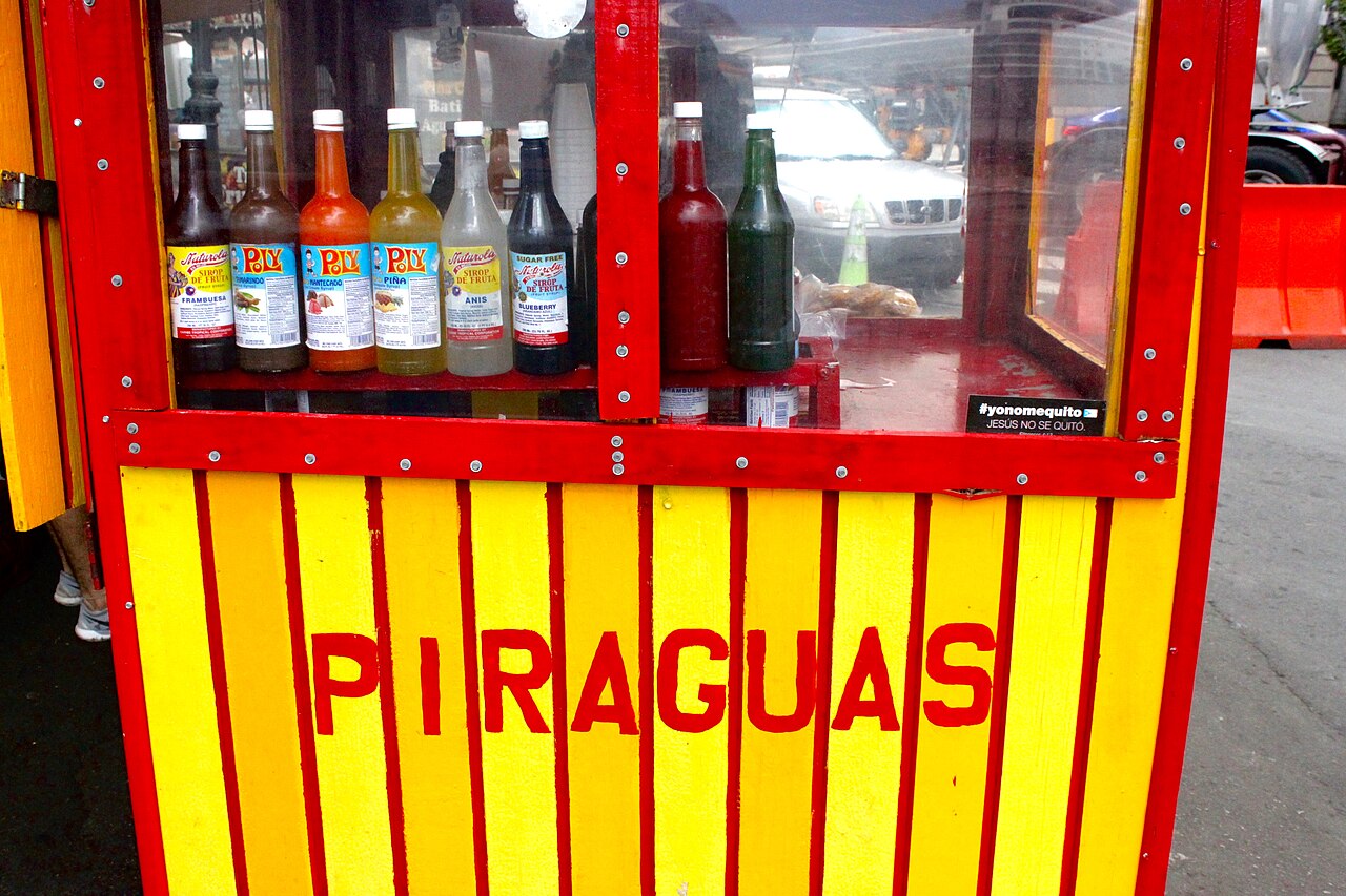 Colorful Puerto Rican piragua cart on a sunny San Juan street with piragüero shaving ice, customers gathered, vibrant scene