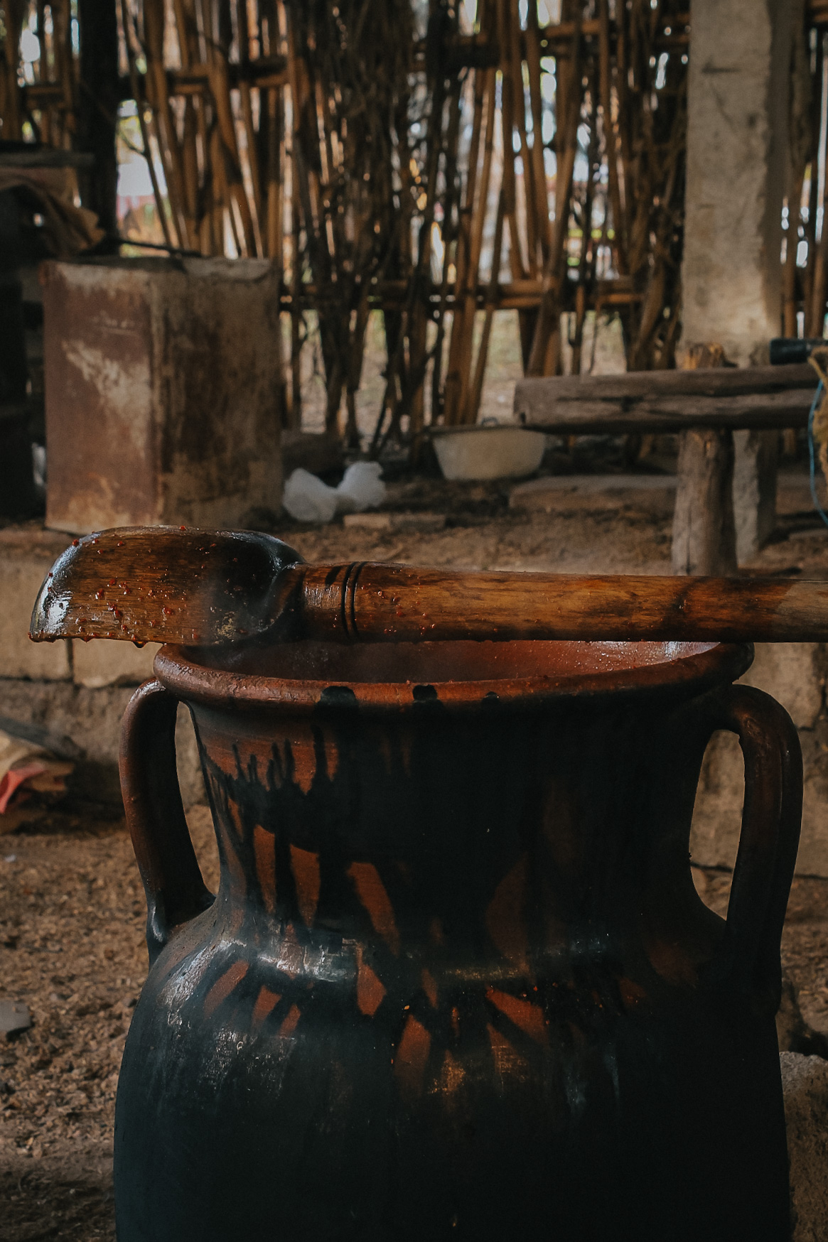Clay olla with wooden spoon stirring coffee mixture, showing rich brown color, cinnamon stick floating, close-up cooking scene