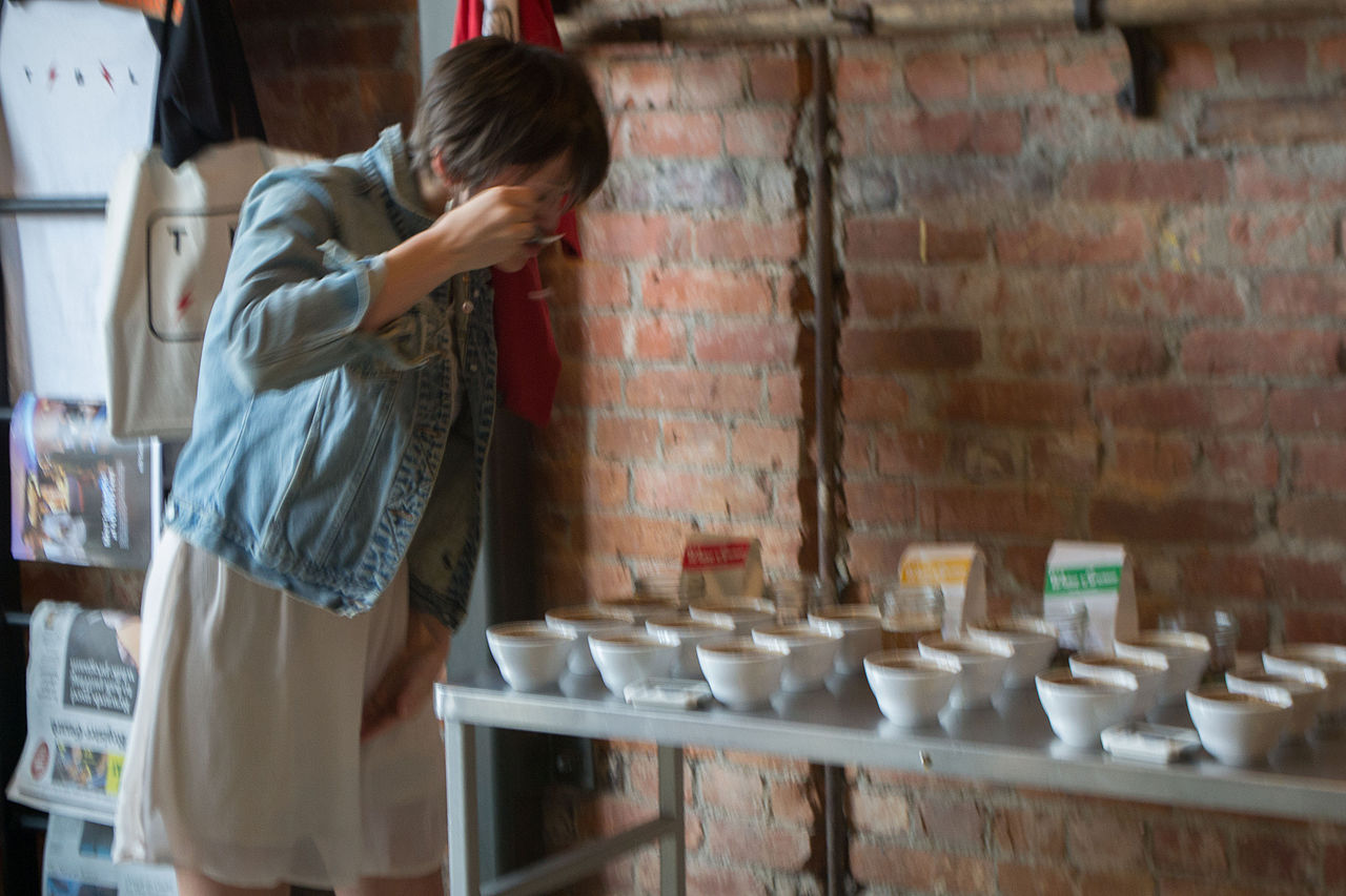 coffee cupping setup with multiple bowls, copper-handled cupping spoons, professional taster examining cups