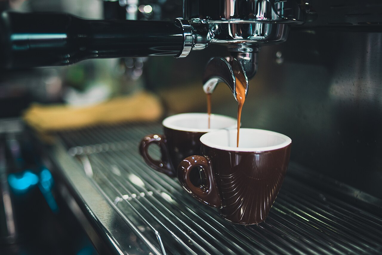 two coffee cups side by side on rustic wooden table, one labeled with Puerto Rico flag colors, both filled with dark coffee, steam rising