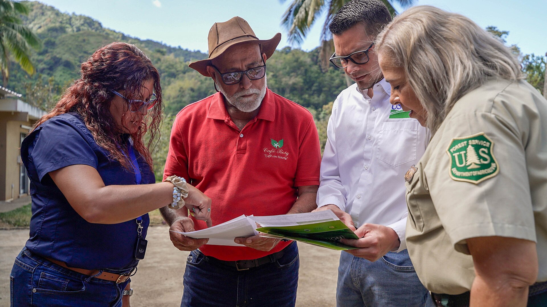 Two women review farm plans alongside a veteran Puerto Rican coffee grower in a Cafe Roig shirt and a USDA forester, on a coffee farm in the Puerto Rico mountains
