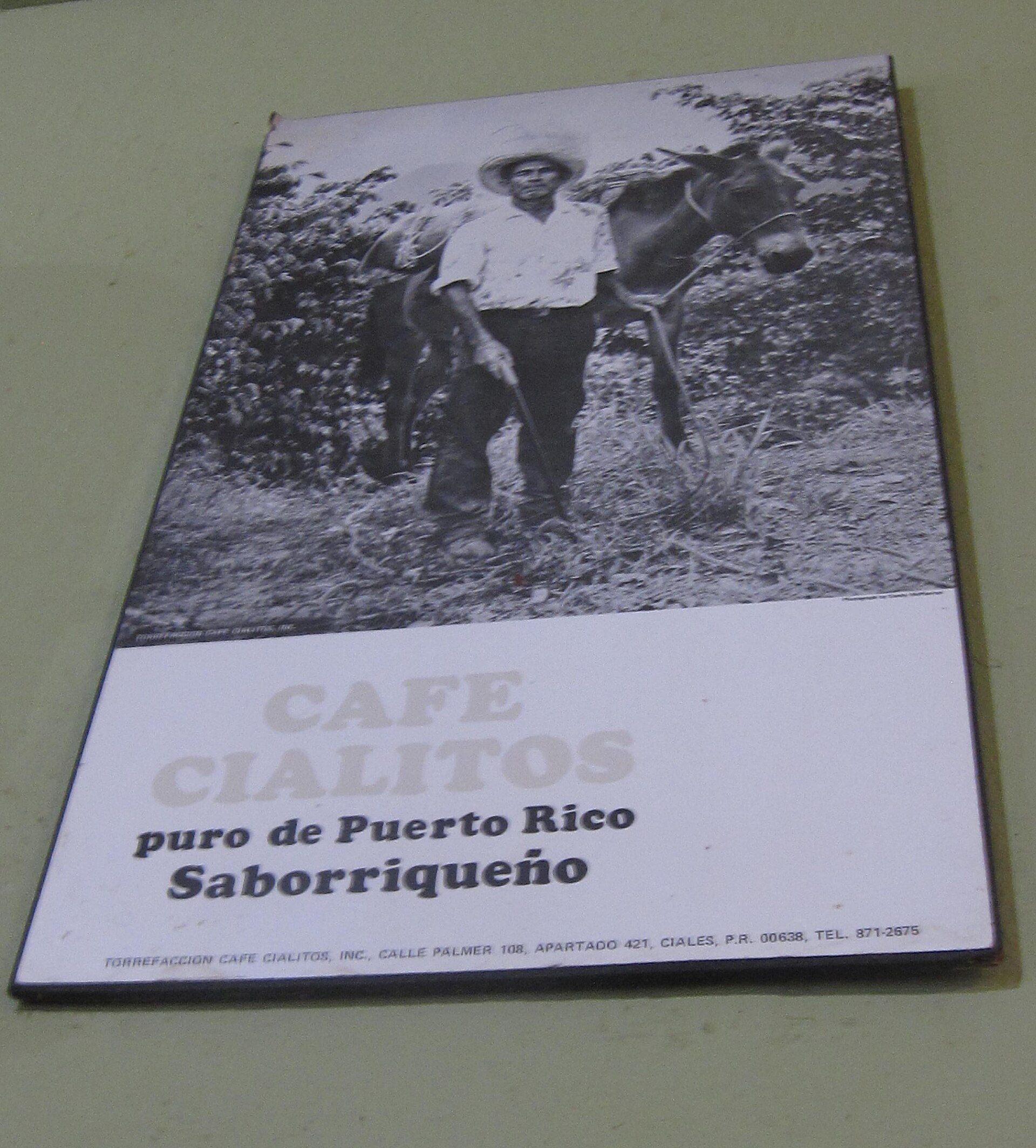 A Cafe Cialitos placard reading puro de Puerto Rico, Saborriqueno, above an archival photograph of a Puerto Rican coffee farmer with his mule