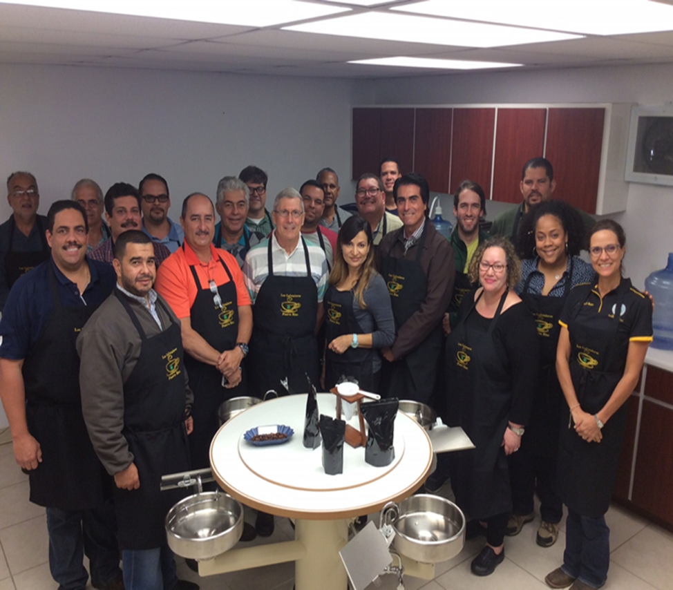 A coffee cupping laboratory during a training session: cupping table, sample bags and spittoons, with participants seated around the table.