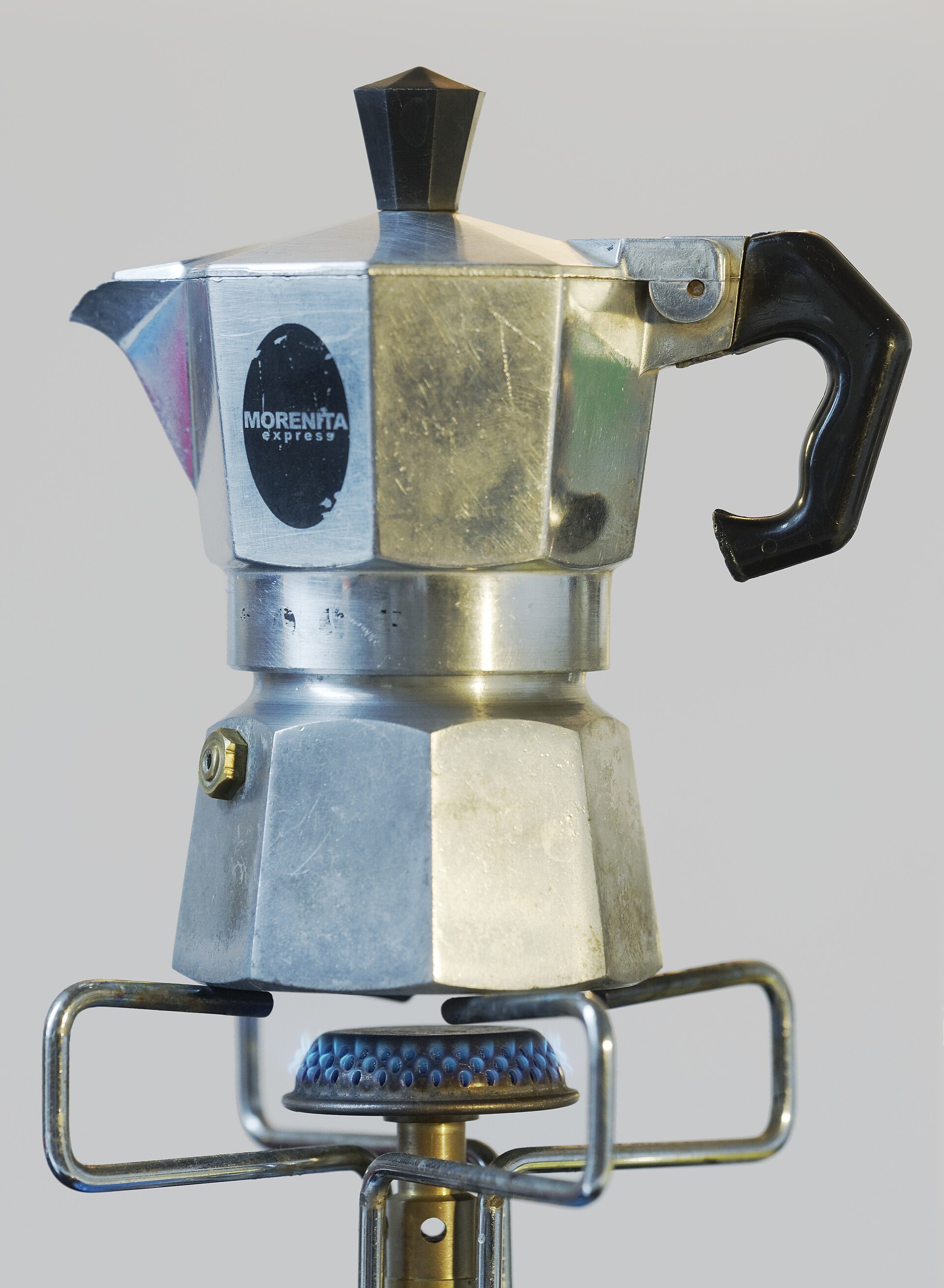 An aluminium stovetop cafetera sitting on a lit gas burner, the everyday way strong coffee is brewed at home