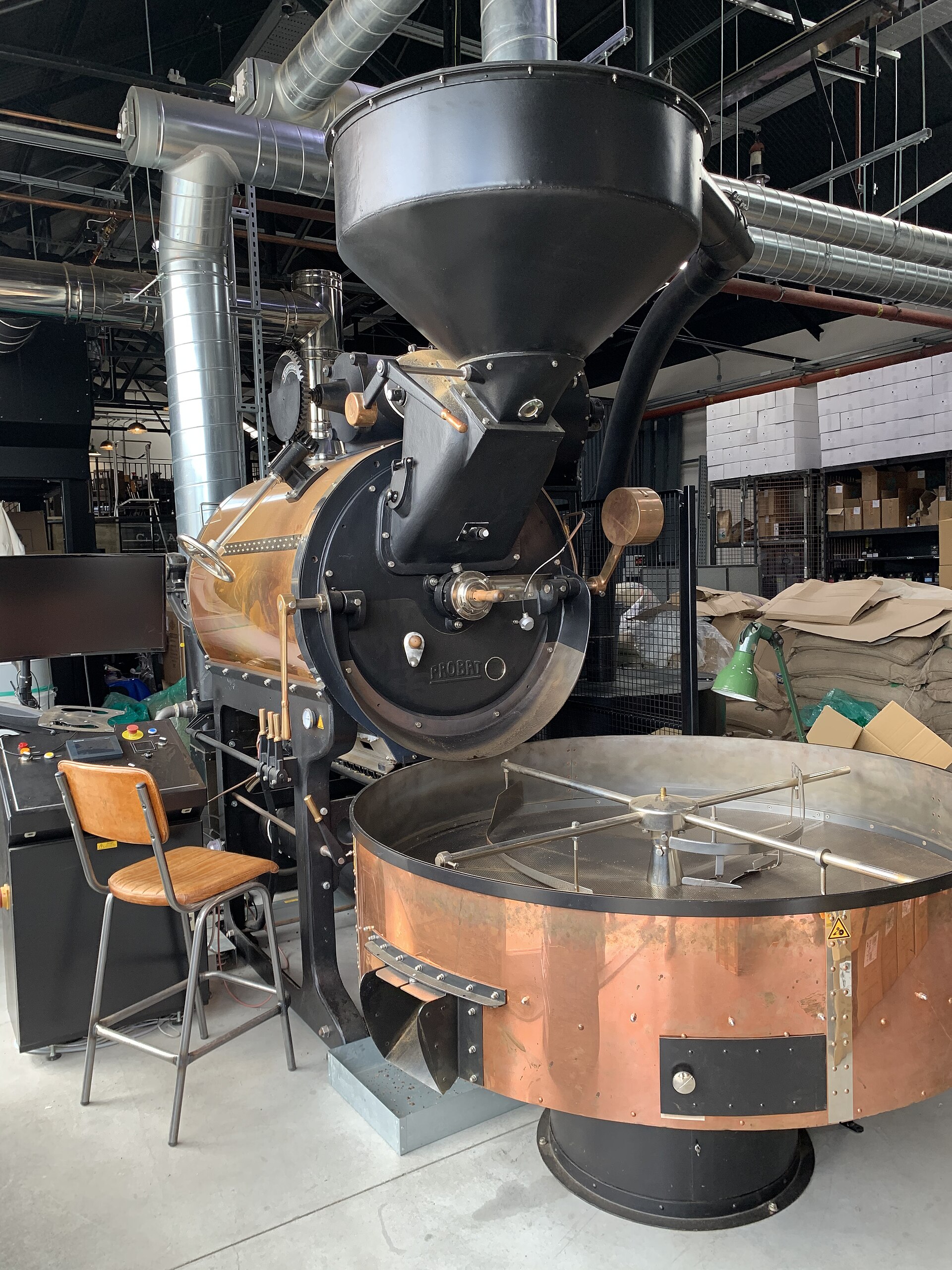 Commercial Probat drum coffee roaster with copper cooling tray and extraction ducting in a working roastery