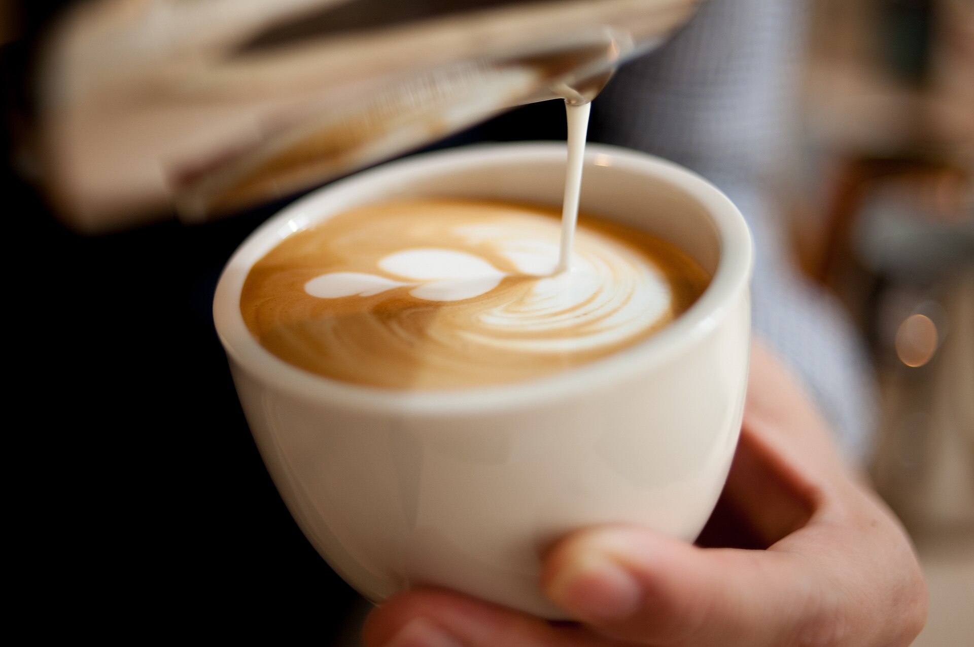 A barista pouring a tulip latte-art pattern into a white ceramic cappuccino cup