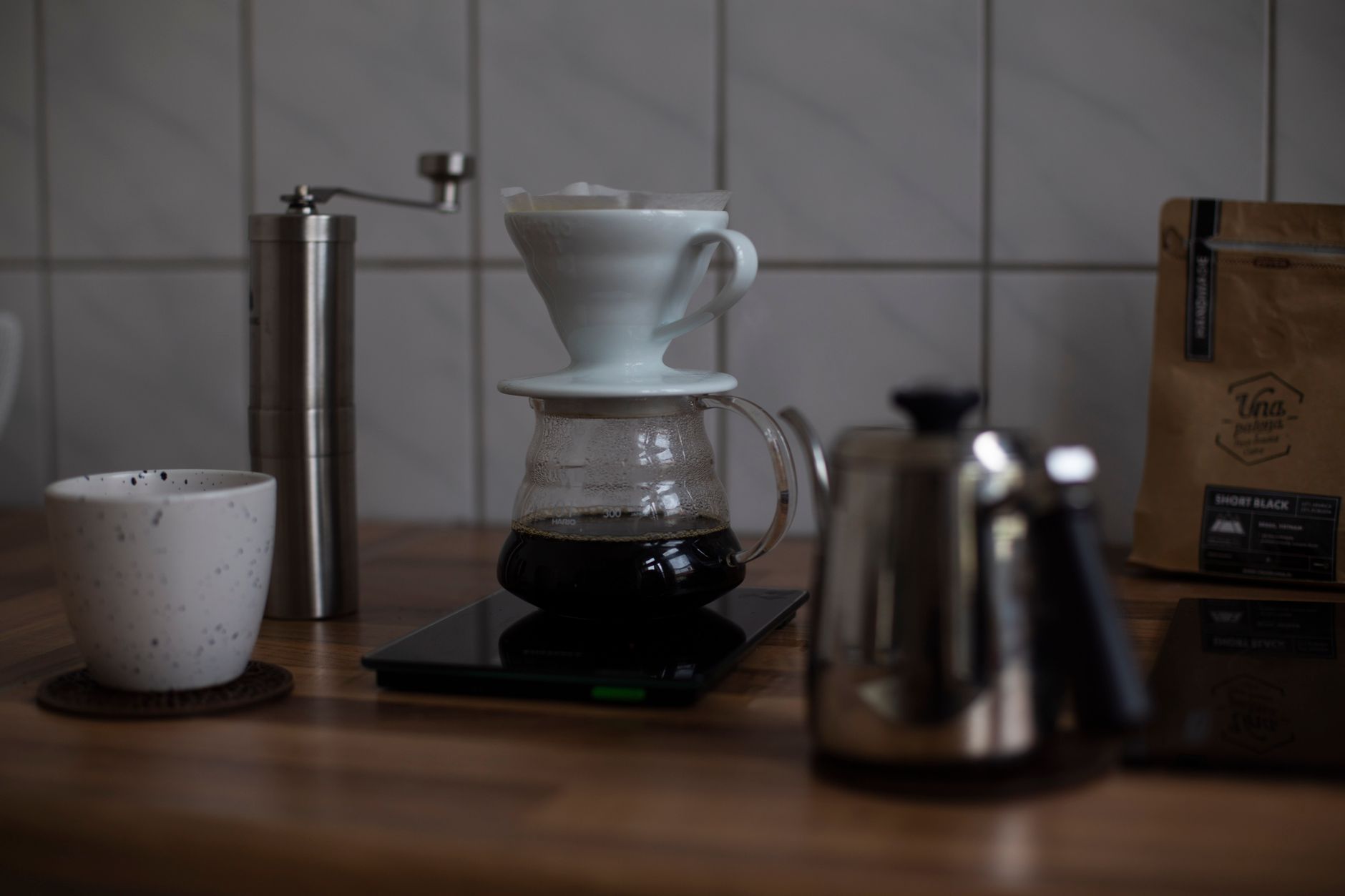 A pour-over brewer on a digital scale during a timed brew, with grinder and kettle