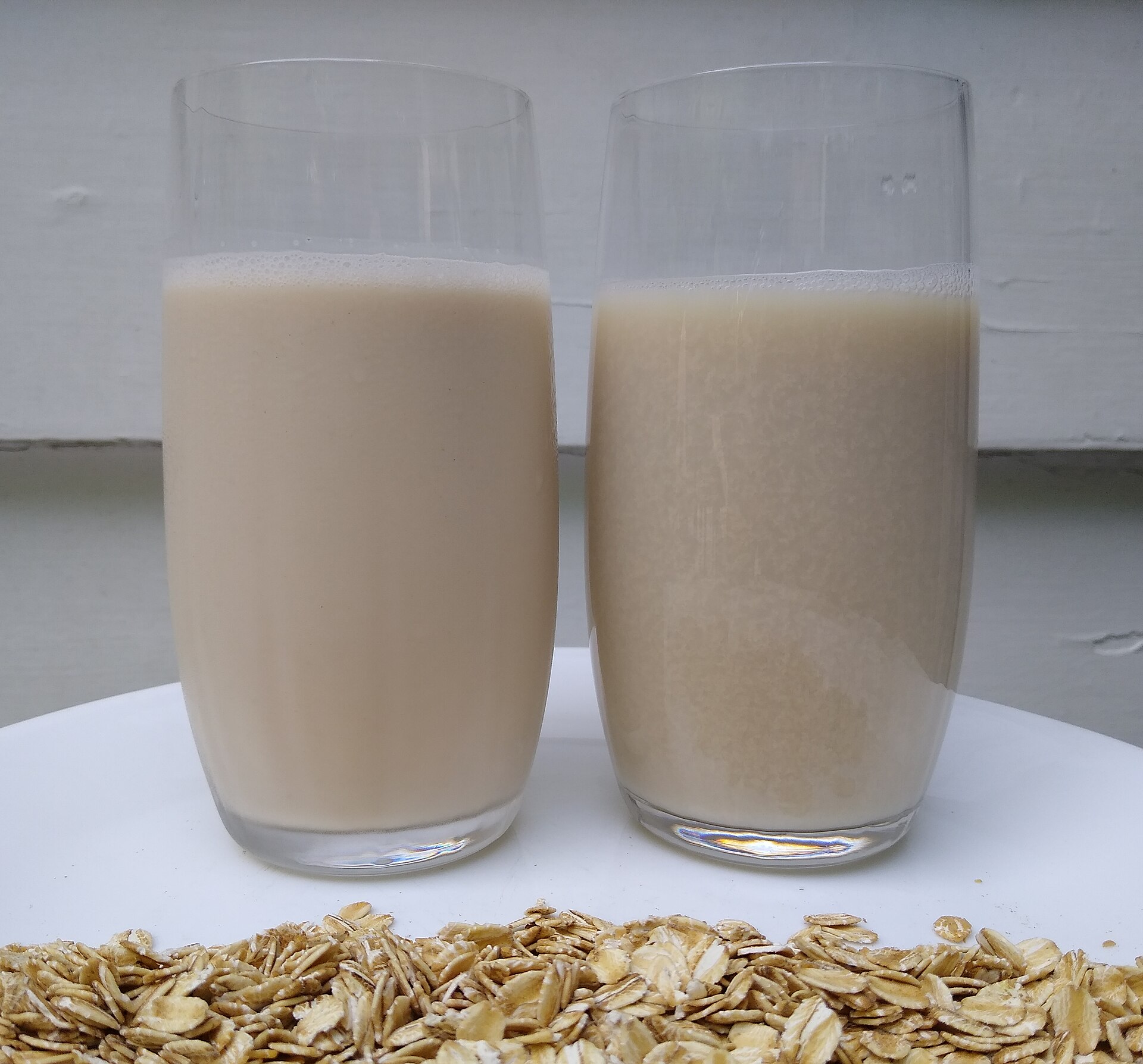 Two glasses of oat milk beside rolled oats, the most common dairy alternative used for steaming