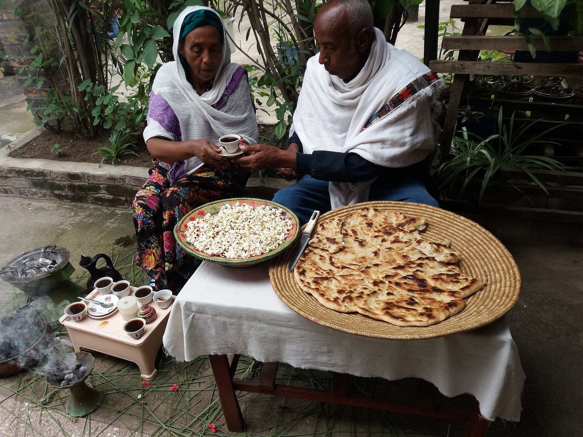 A woman serving coffee from the jebena during an Ethiopian coffee ceremony, with popcorn and bread