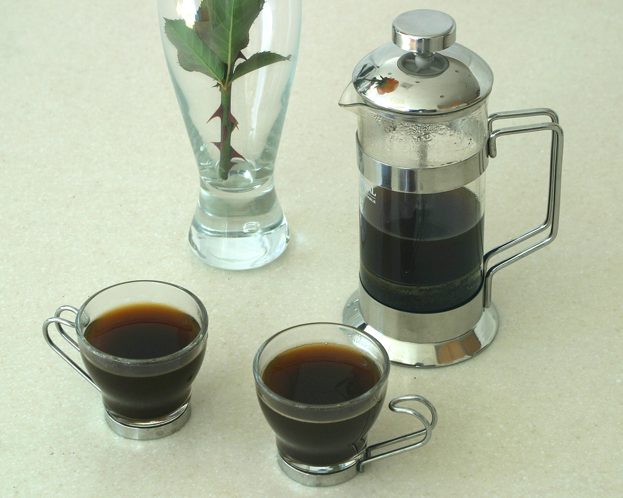 A stainless steel and glass French press with freshly pressed coffee and two cups