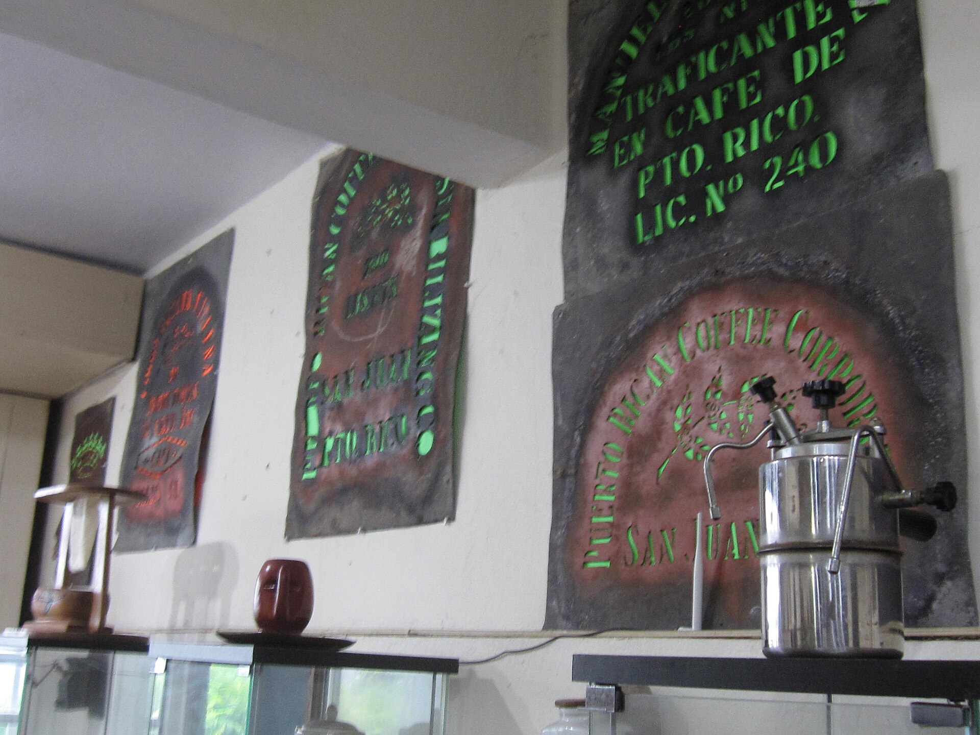 A vintage Puerto Rican stovetop coffee maker below historic coffee-sack stencils reading Puerto Rican Coffee Corporation, San Juan, at the Coffee Museum in Ciales