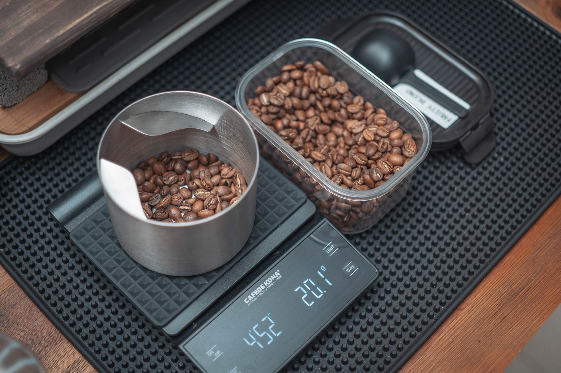 A stainless dosing cup of coffee beans on a digital brewing scale reading 20.1 grams