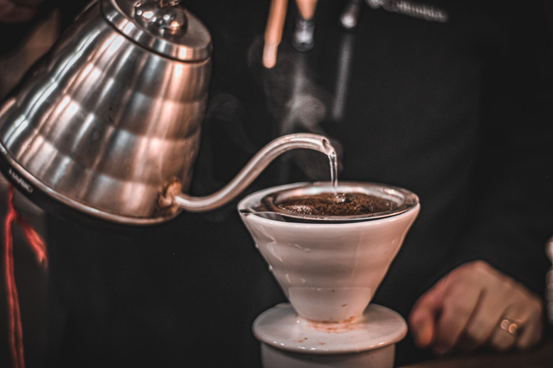 A stainless gooseneck kettle pouring a thin steady stream into a pour-over cone