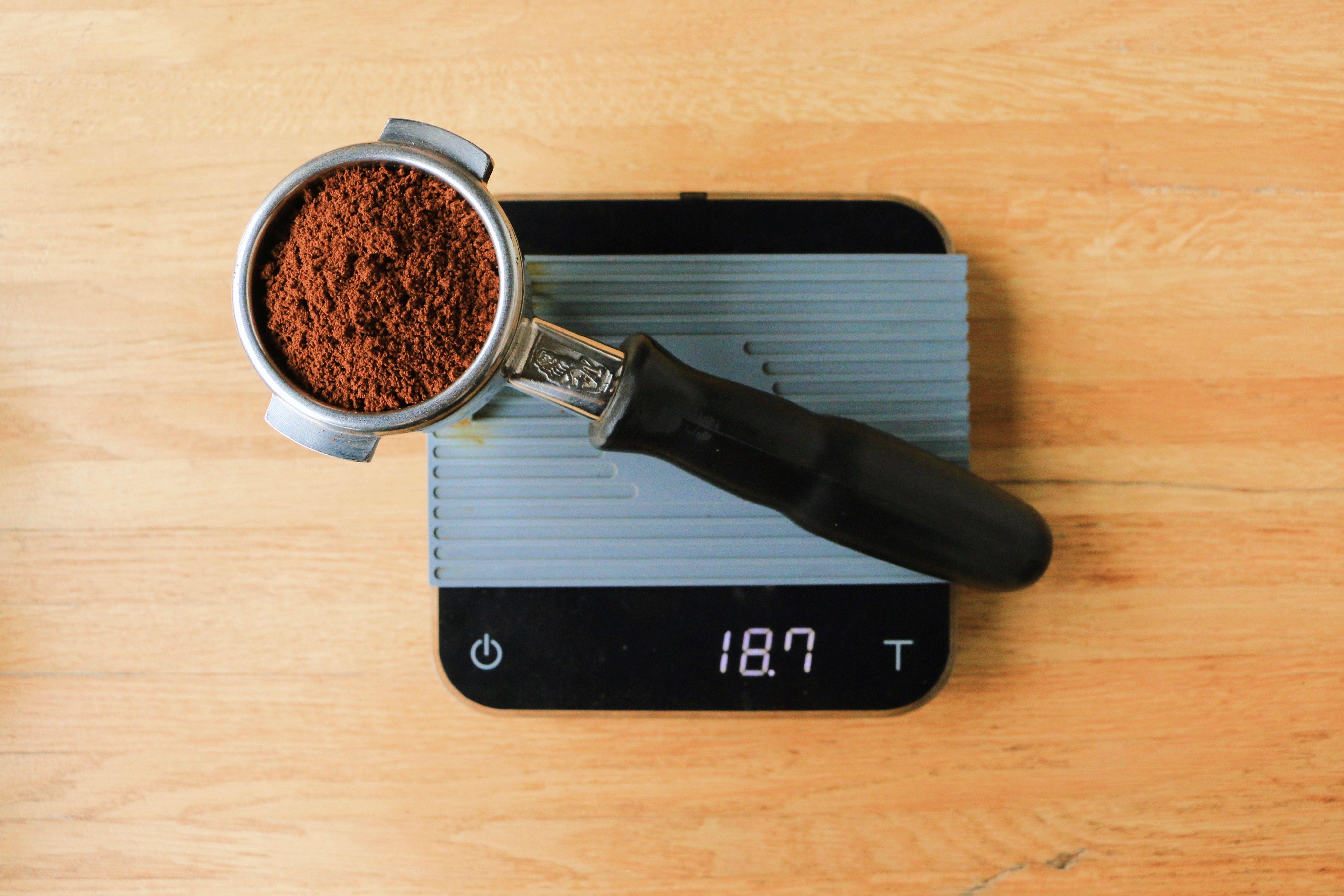 A portafilter of ground coffee resting on a digital scale, the display reading 18.7 grams.