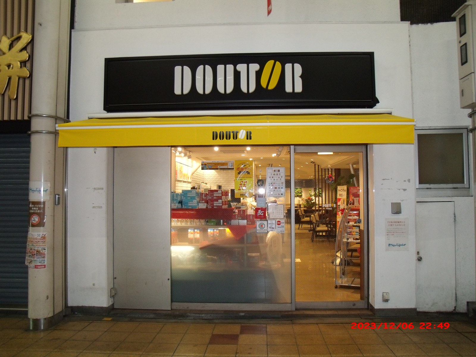 A Doutor Coffee shop in Senbayashi, Asahi-ku, Osaka, with the chain's name on the sign and on the yellow awning, photographed at night in 2023.