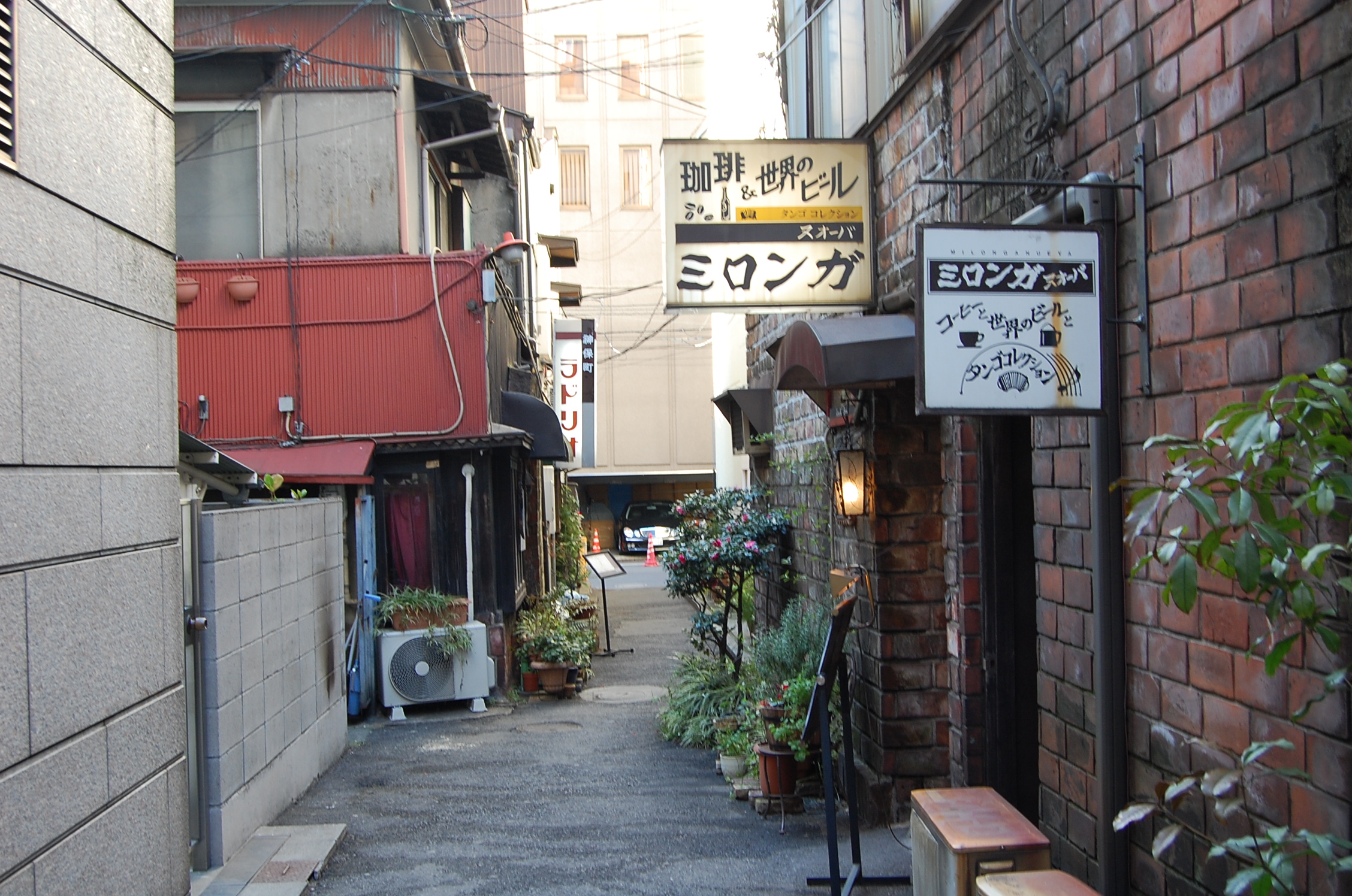 Milonga Nueva, a kissaten in a narrow brick-walled alley in Jinbocho, Tokyo, its signs offering coffee, world beers and a tango collection; the sign of Ladrio hangs further along the alley.