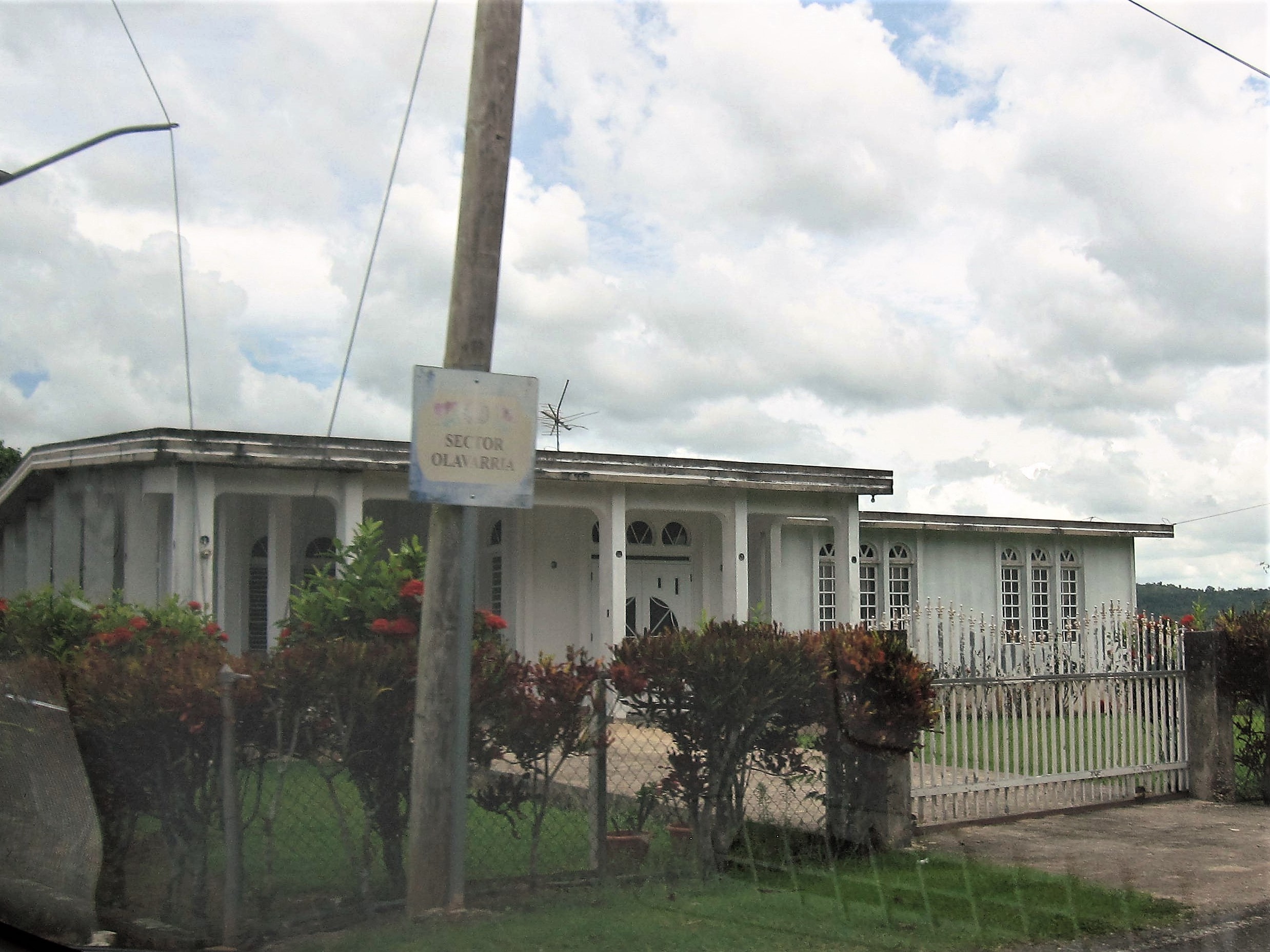 A single-storey house with a colonnaded porch beside a utility pole signed Sector Olavarría, in Perchas 2, San Sebastián